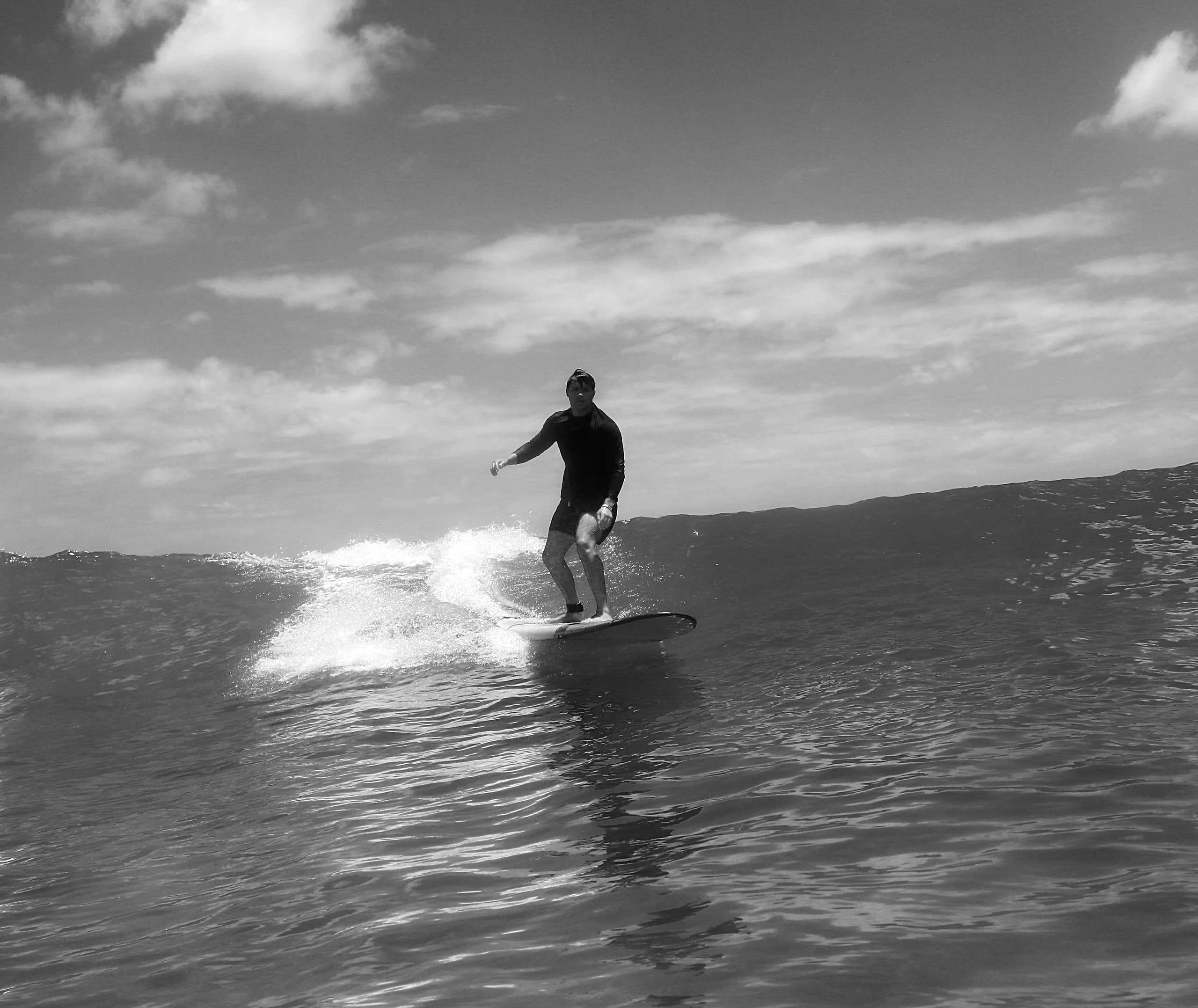 A surfer riding along the face of a wave, in black and white.