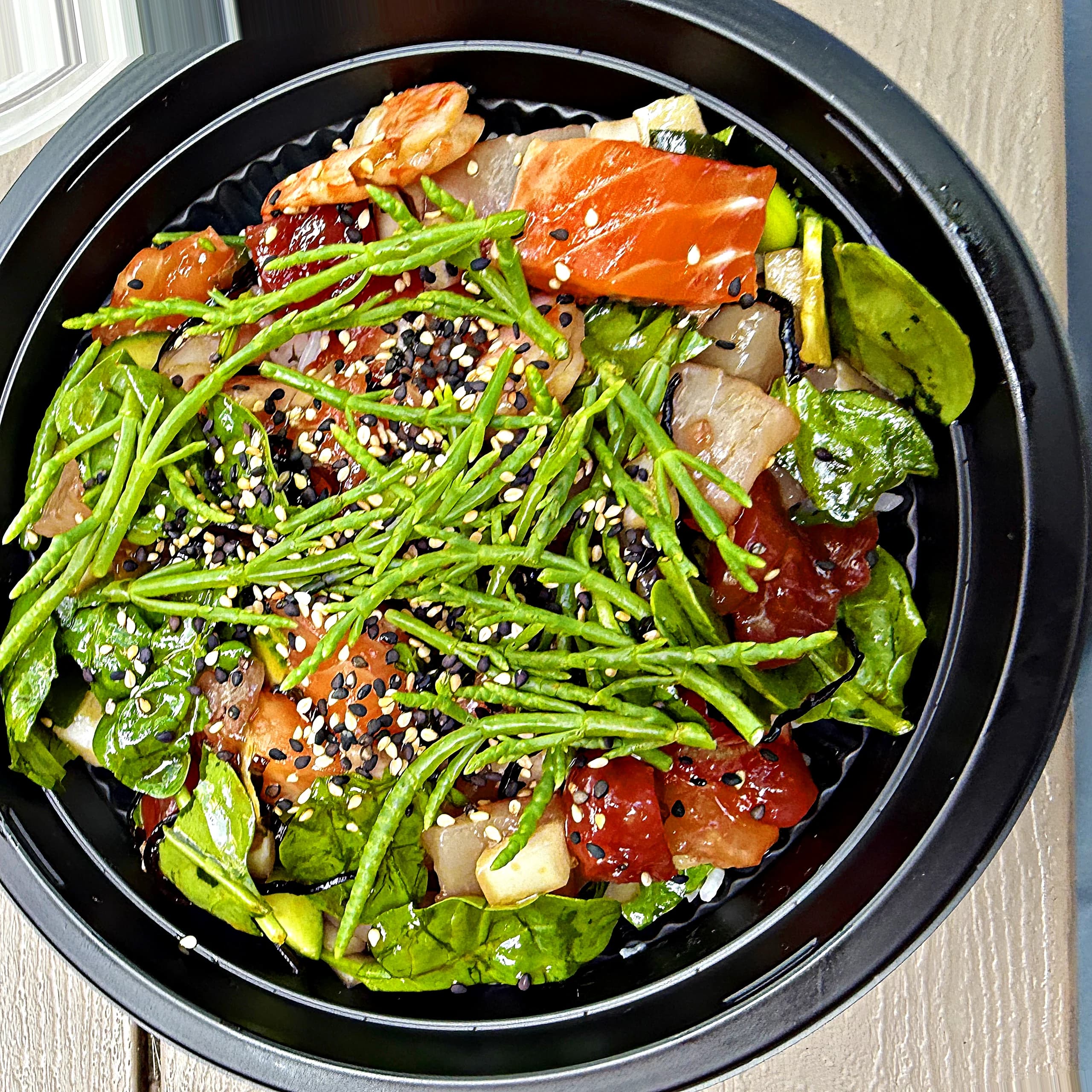 An overhead shot of a poke bowl with tuna, salmon, avocado and sea beans, sesame scattered across the top.