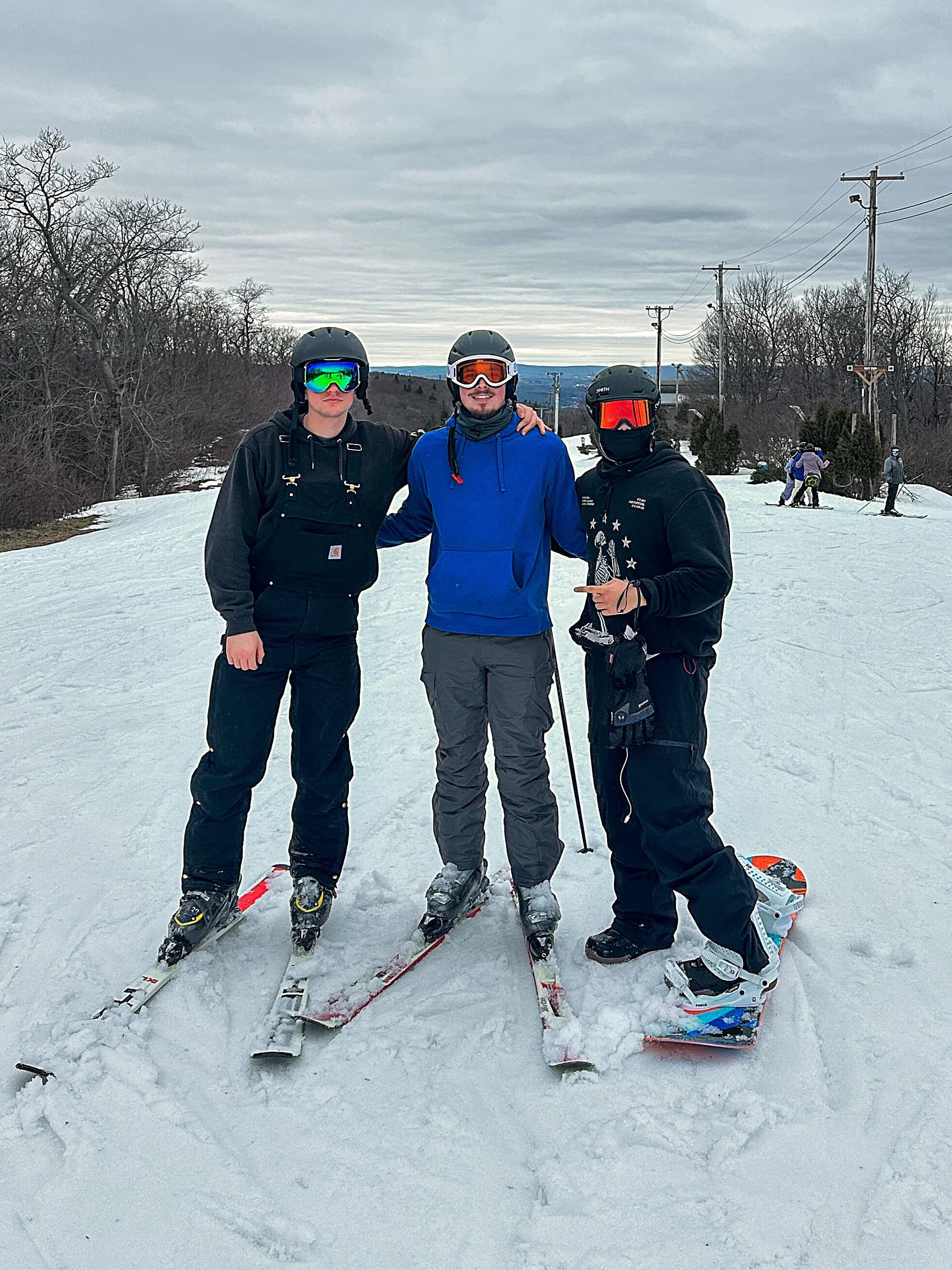 Three people in ski and snowboard gear standing together on a snowy slope under a bright sky.