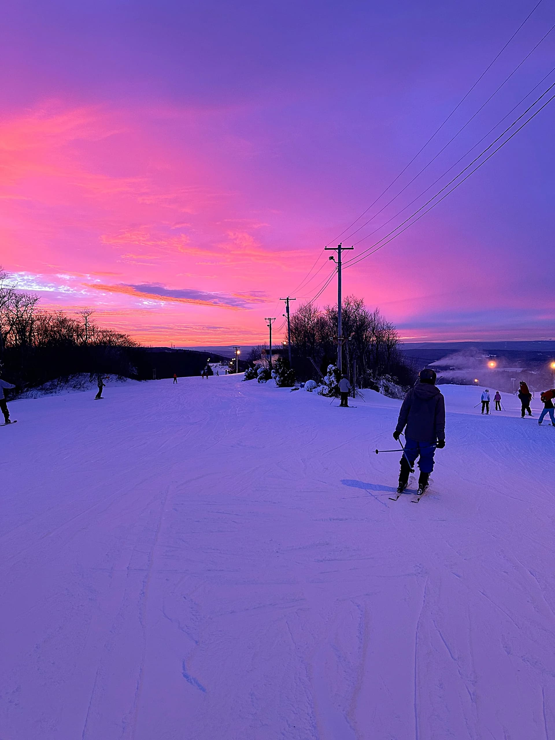 A snowy slope under a pink and purple sunset, a snowboarder riding down in the foreground.