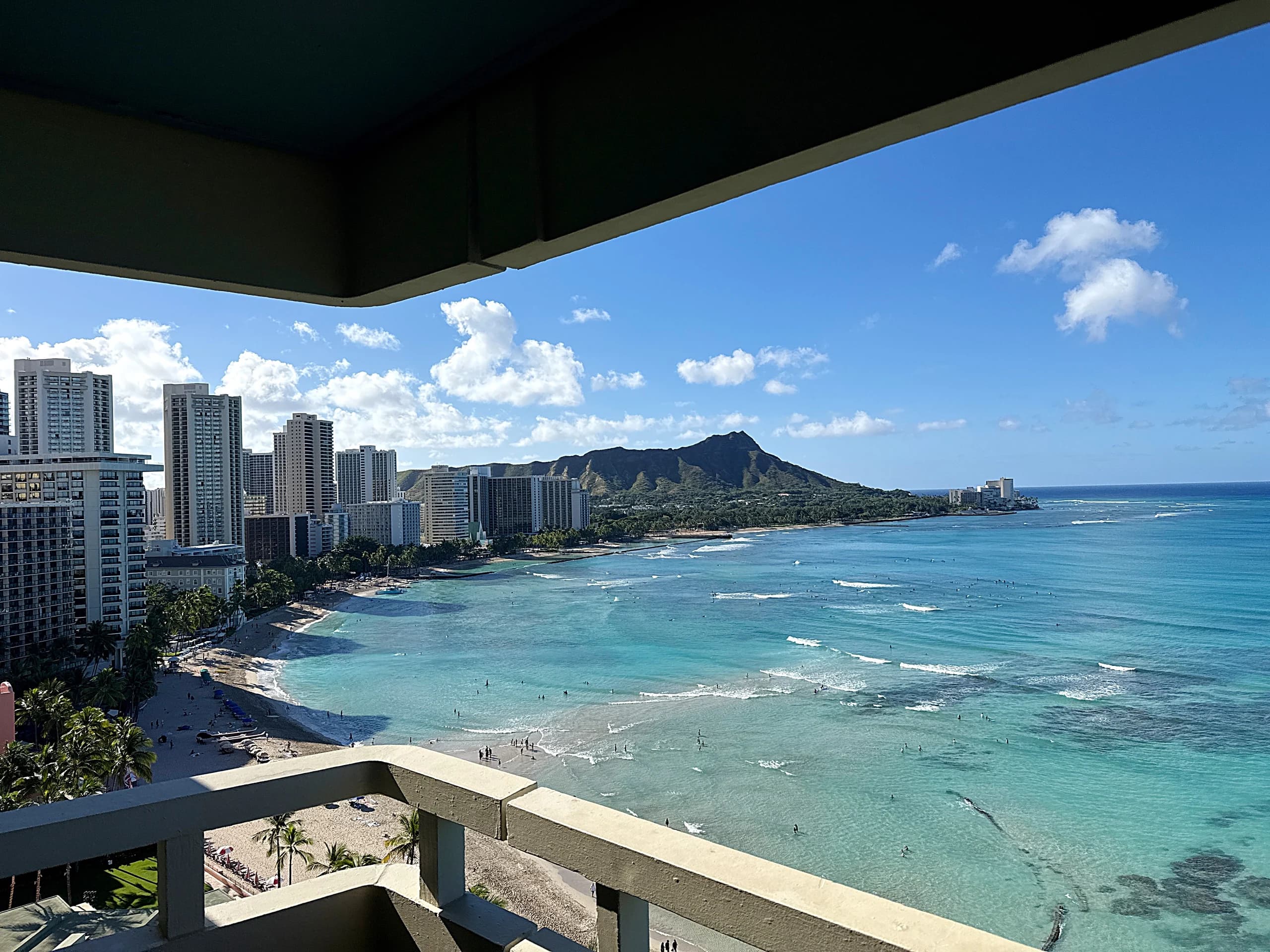 Waikīkī beach and Diamond Head seen from a high balcony, turquoise water and breaking surf below.